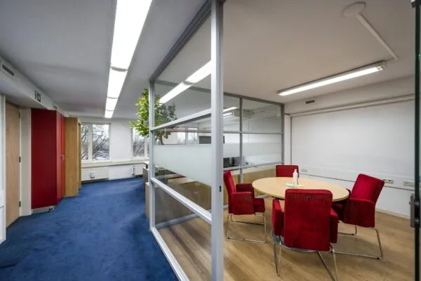 Vergaderruimte met glazen wanden, rode stoelen en een ronde tafel in een modern kantoorpand aan de Prins Hendrikkade.